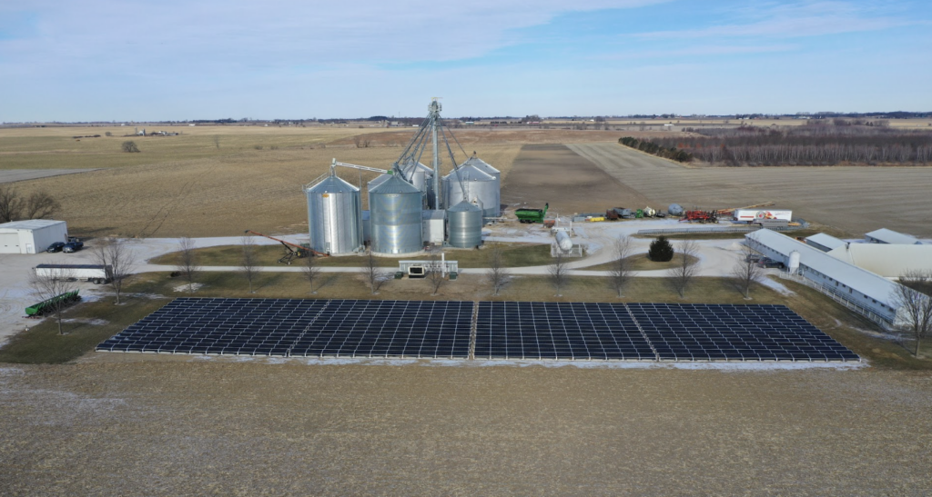 Aerial view of an Illinois farm featuring solar panels, grain silos, and agricultural equipment, highlighting the benefits of solar energy for farming operations.